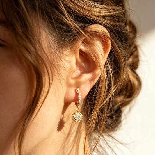 Gold clip-on hoop earrings with pave cubic zirconia pavé detailing, dangling celestial sunburst charms, and clear round silicone comfort backings.