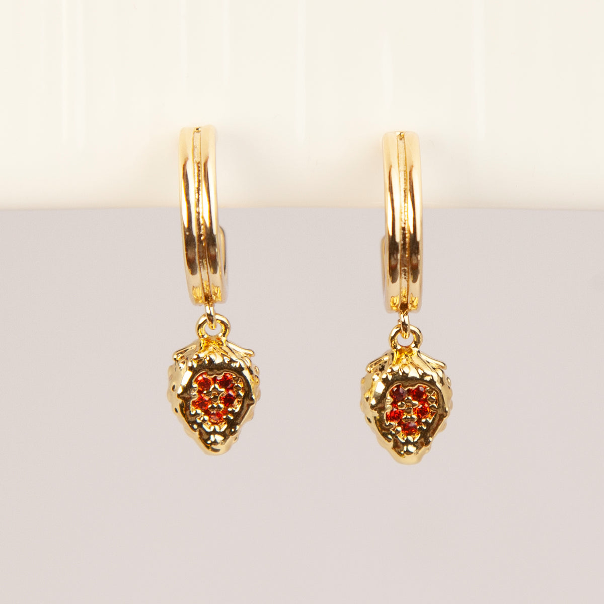 Gold clip-on hoop earrings featuring textured strawberry pendants set with sparkling red crystals and clear cushion backings.