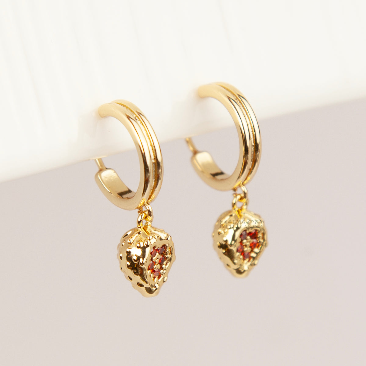 Gold clip-on hoop earrings featuring textured strawberry pendants set with sparkling red crystals and clear cushion backings.