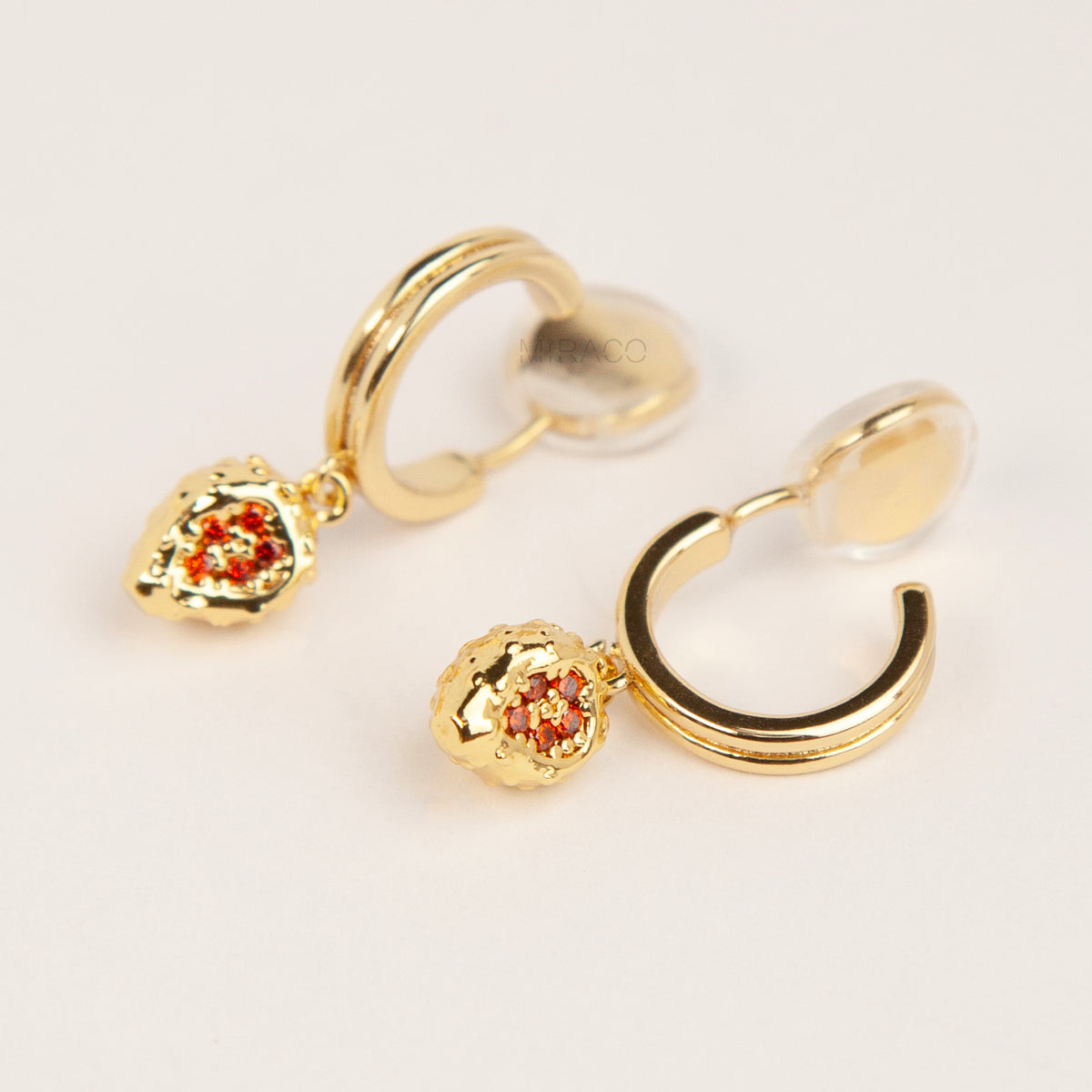 Gold clip-on hoop earrings featuring textured strawberry pendants set with sparkling red crystals and clear cushion backings.