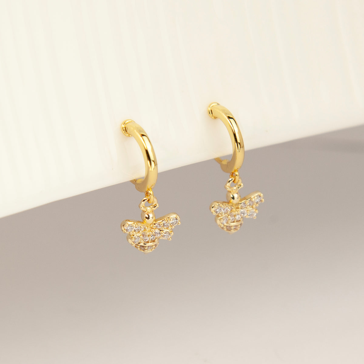 Gold clip-on hoop earrings with a sparkling cubic zirconia pave bumblebee charm and comfortable round cushion backings.