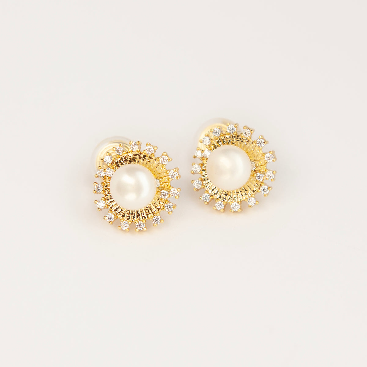 Gold clip-on stud earrings featuring a central freshwater pearl framed by a pavé cubic zirconia sunburst halo with round cushioned coil backs.