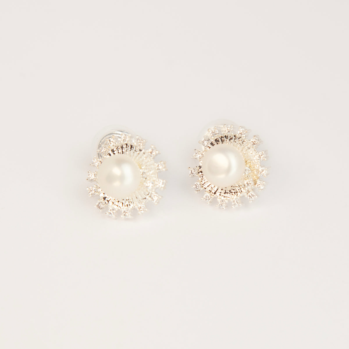 silver clip-on stud earrings featuring a central freshwater pearl framed by a pavé cubic zirconia sunburst halo with round cushioned coil backs.