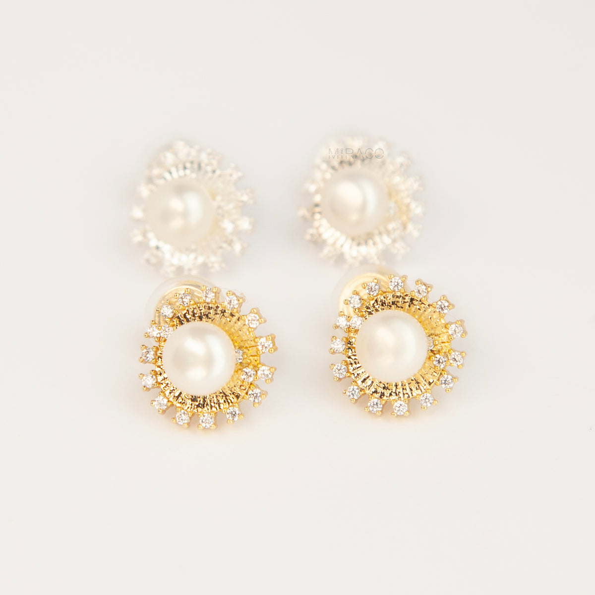 Gold and silver clip-on stud earrings featuring a central freshwater pearl framed by a pavé cubic zirconia sunburst halo with round cushioned coil backs.