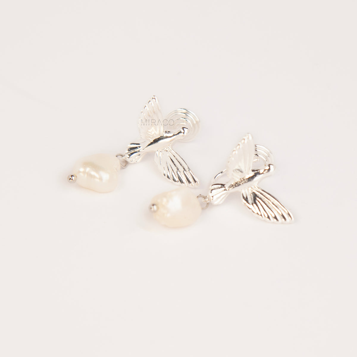 Gold and silver bird clip-on drop earrings featuring detailed flying bird motifs with dangling genuine freshwater baroque pearls on cushioned coil backs.