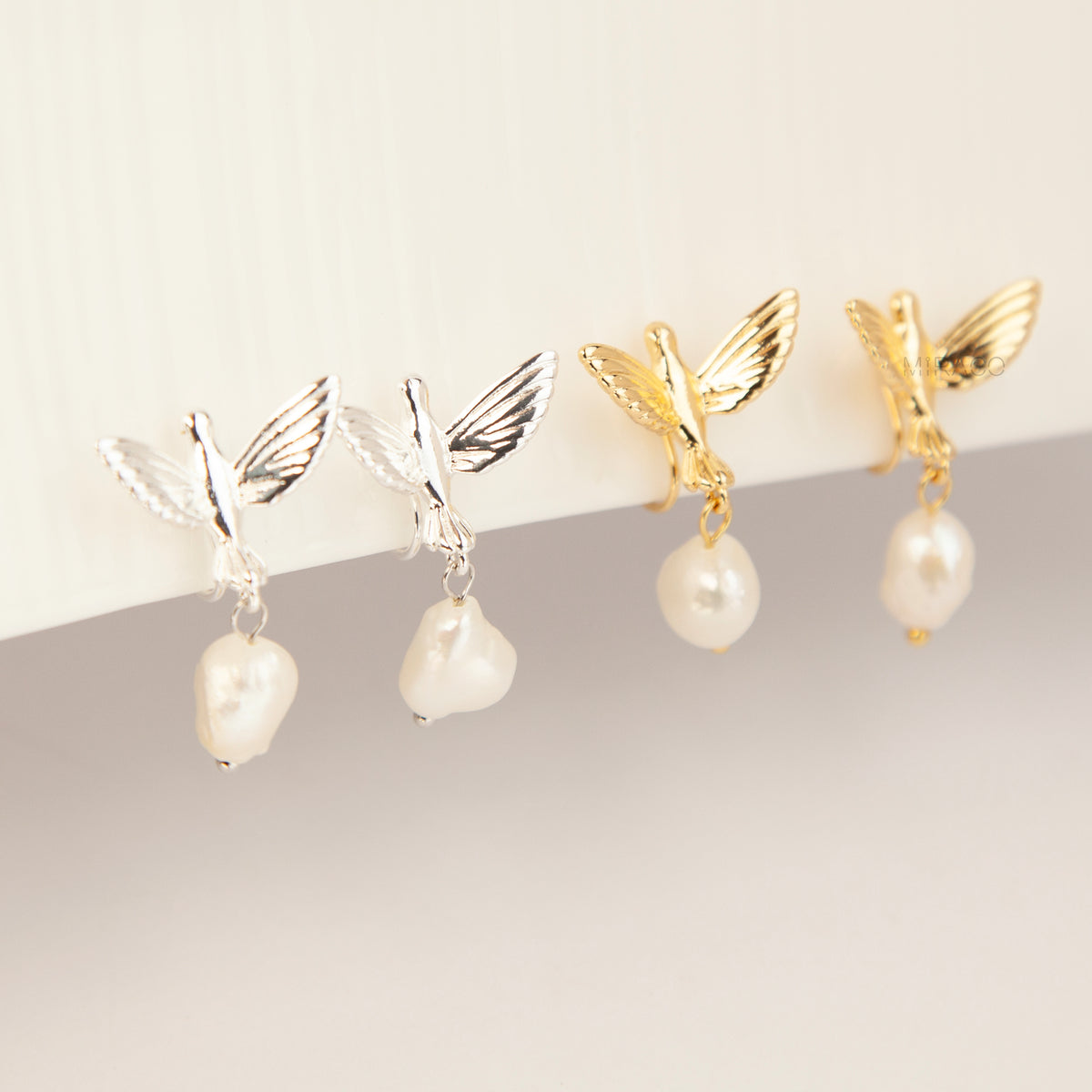 Gold and silver bird clip-on drop earrings featuring detailed flying bird motifs with dangling genuine freshwater baroque pearls on cushioned coil backs.