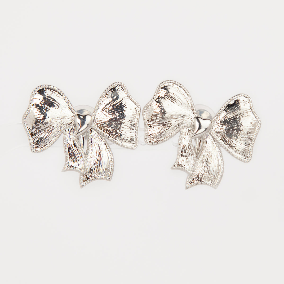 Woman wearing textured silver ribbon bow clip-on earring with a comfortable foldable paddle back for non-pierced ears.