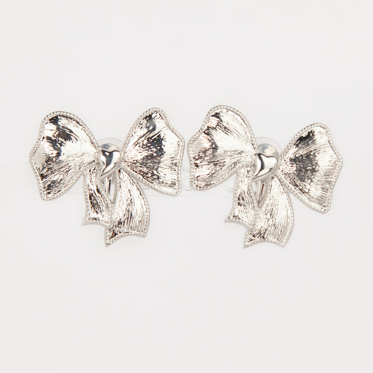 Woman wearing textured silver ribbon bow clip-on earring with a comfortable foldable paddle back for non-pierced ears.