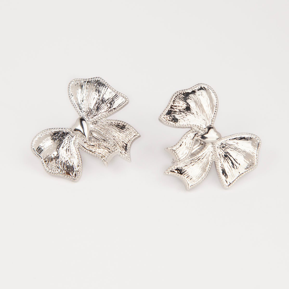 Woman wearing textured silver ribbon bow clip-on earring with a comfortable foldable paddle back for non-pierced ears.