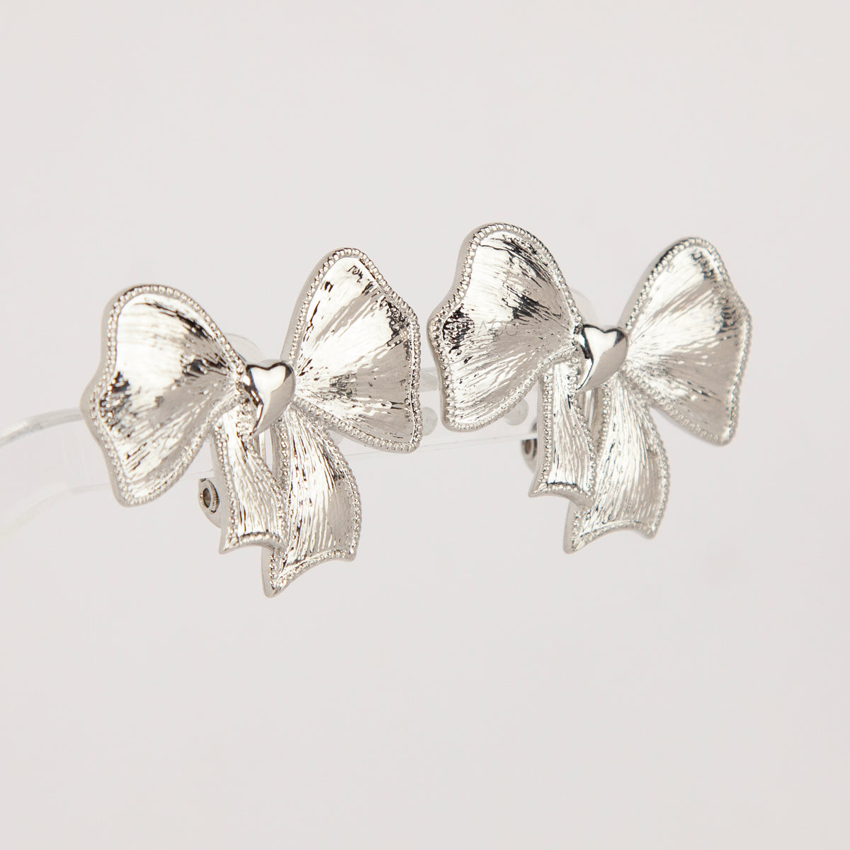 Woman wearing textured silver ribbon bow clip-on earring with a comfortable foldable paddle back for non-pierced ears.