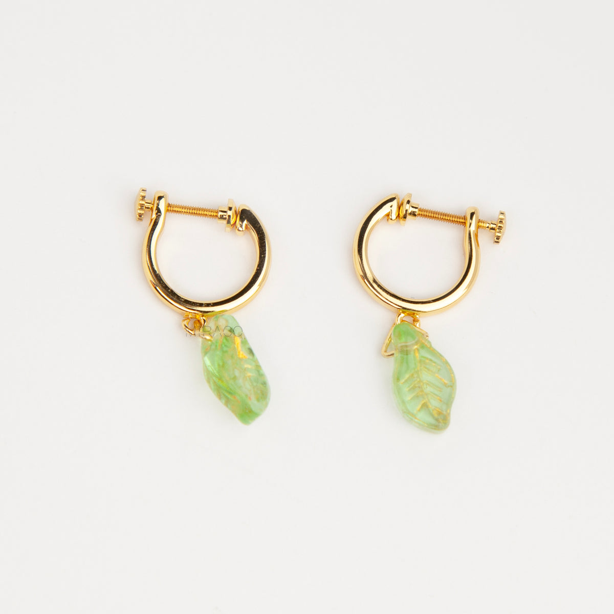 gold clip-on hoop earrings with light green carved glass leaf drops featuring an adjustable screw back for non-pierced ears.