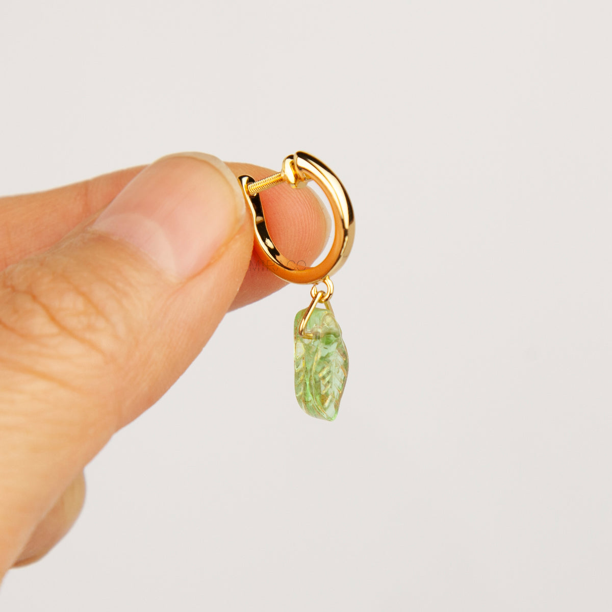 gold clip-on hoop earrings with light green carved glass leaf drops featuring an adjustable screw back for non-pierced ears.