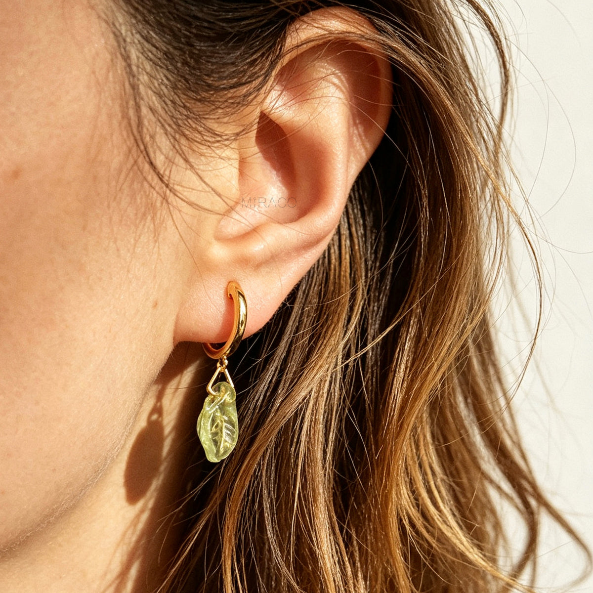 gold clip-on hoop earrings with light green carved glass leaf drops featuring an adjustable screw back for non-pierced ears.