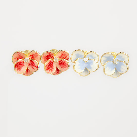 Four small flower-shaped stud earrings on a plain light background. Two earrings have coral-pink and red enamel petals with a gold-tone outline and clear center stones, and two have pale blue and white enamel petals with gold-tone outlines and clear center stones.