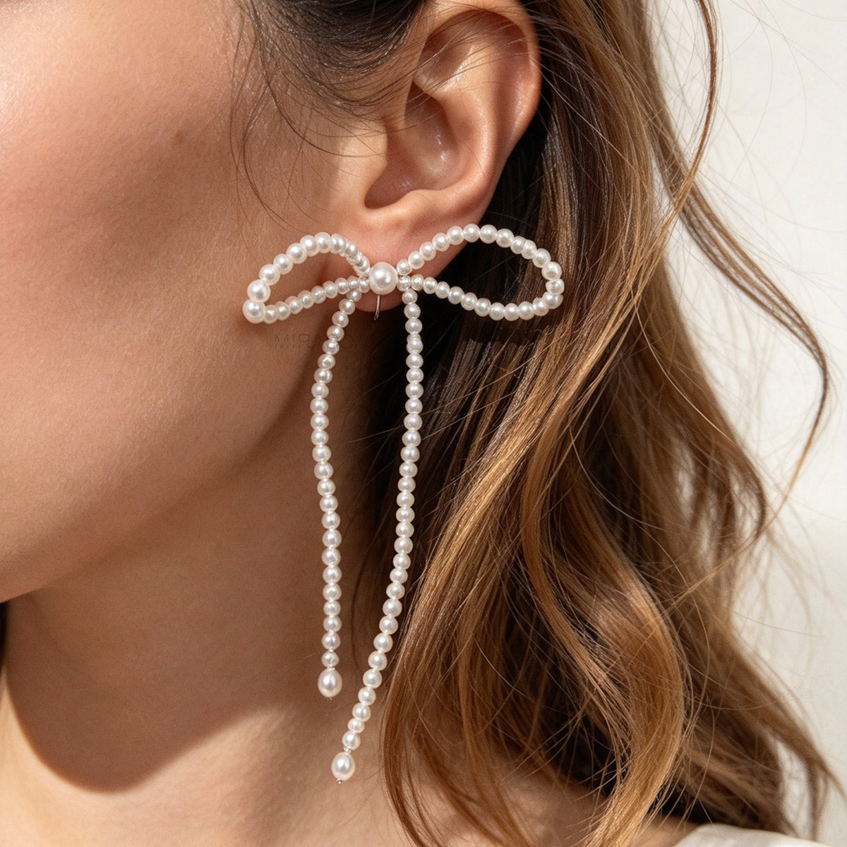 Woman wearing long cascading pearl bow clip-on dangle earrings with silver spring coil backs for non-pierced ears.