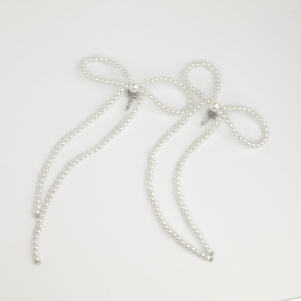 long cascading pearl bow clip-on dangle earrings with silver spring coil backs for non-pierced ears.