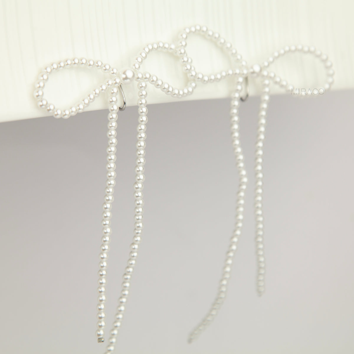 long cascading pearl bow clip-on dangle earrings with silver spring coil backs for non-pierced ears.