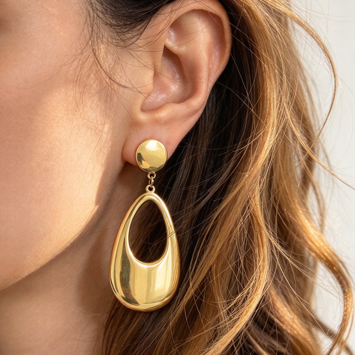 Woman wearing bold gold-plated stainless steel hollow teardrop clip-on dangle earrings with discreet mini-clip backs for non-pierced ears.