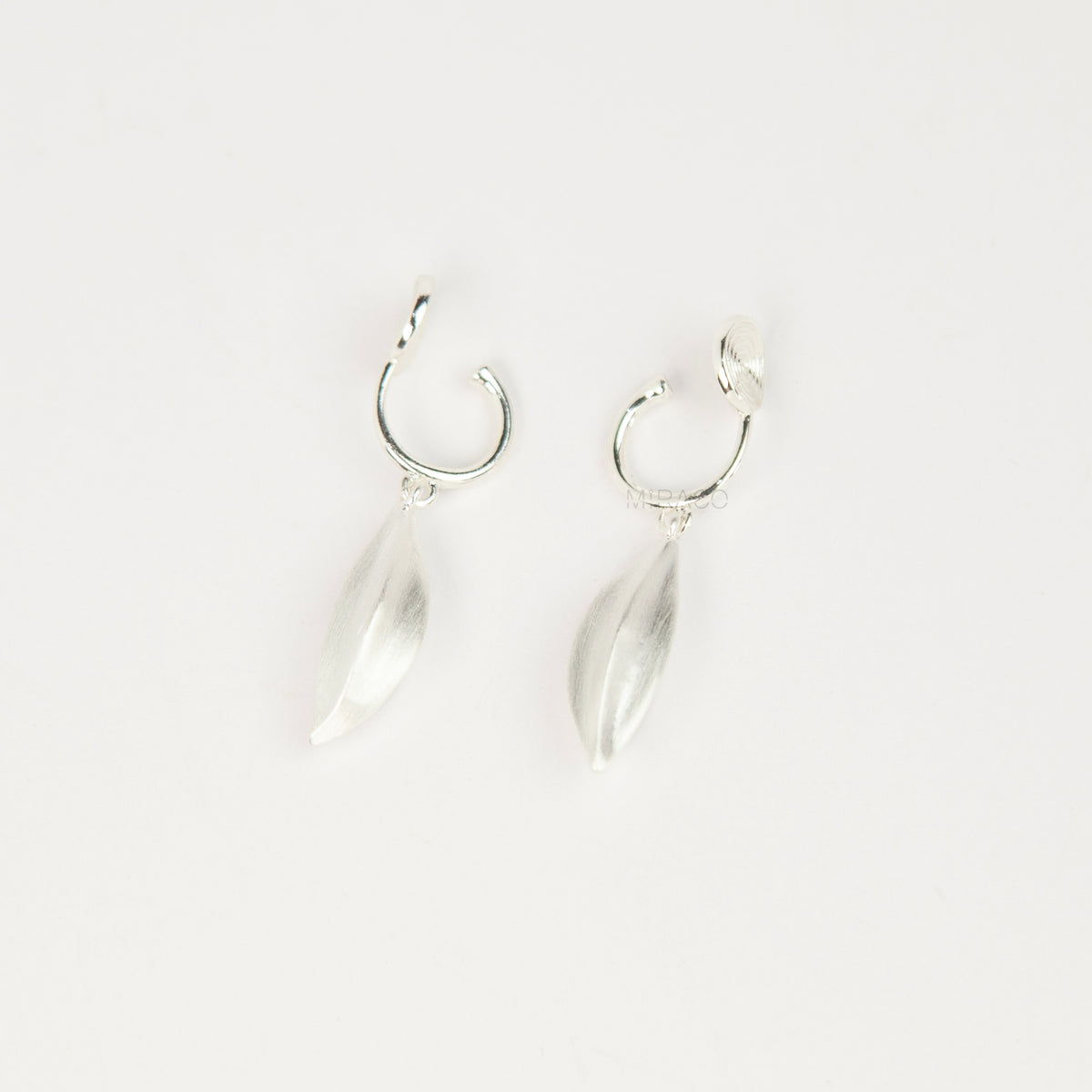 silver clip-on hoop earrings with brushed leaf drop pendants featuring a spring coil back for non-pierced ears.