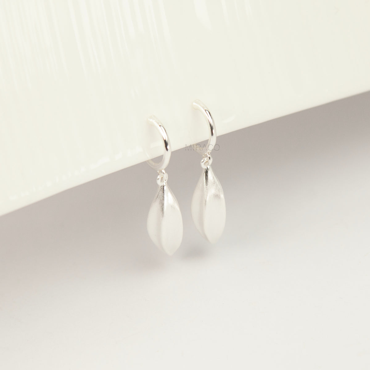 silver clip-on hoop earrings with brushed leaf drop pendants featuring a spring coil back for non-pierced ears.