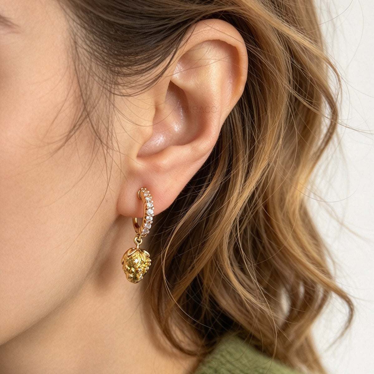 Woman wearing gold-plated strawberry clip-on hoop earrings with pavé cubic zirconia and a comfortable coil back for non-pierced ears.