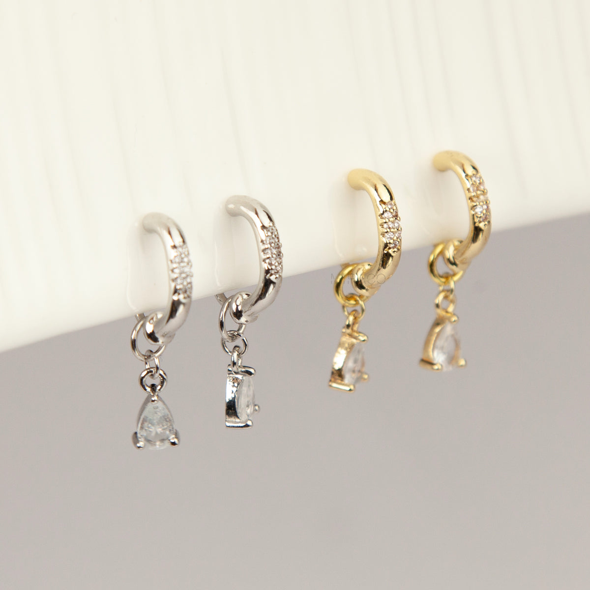 Gold and silver huggie clip-on hoop earrings with pavé cubic zirconia and teardrop CZ drop pendants featuring coil backs for non-pierced ears.