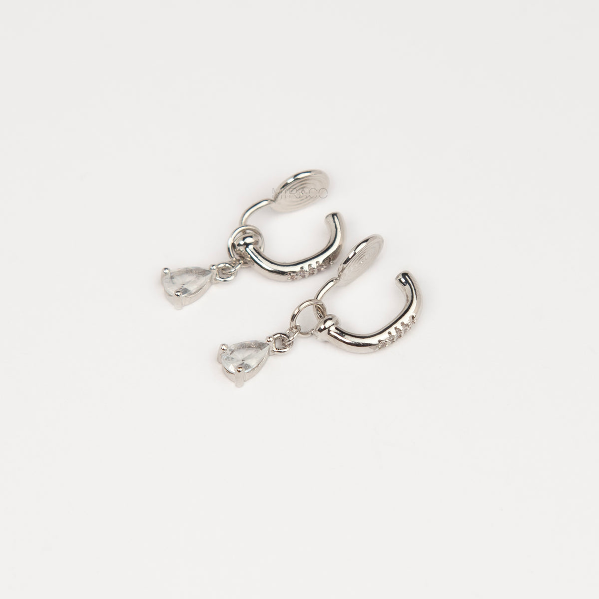 Gold and silver huggie clip-on hoop earrings with pavé cubic zirconia and teardrop CZ drop pendants featuring coil backs for non-pierced ears.