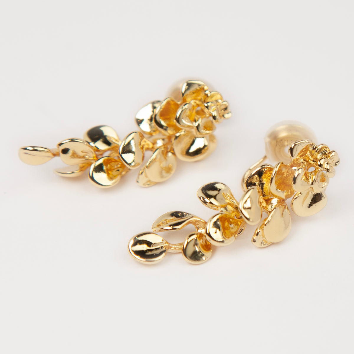 Gold cascading petal drop clip-on earrings with coil-back clips worn on a model's ear.