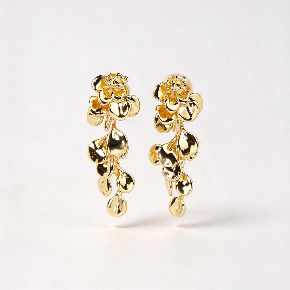 Gold cascading petal drop clip-on earrings with coil-back clips worn on a model's ear.