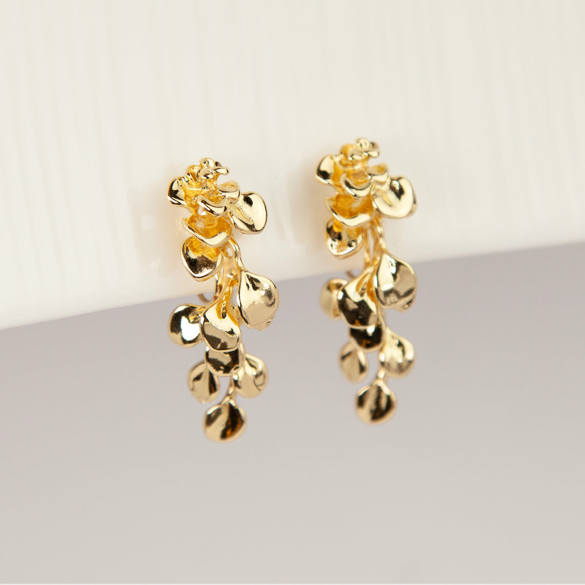 Gold cascading petal drop clip-on earrings with coil-back clips worn on a model's ear.