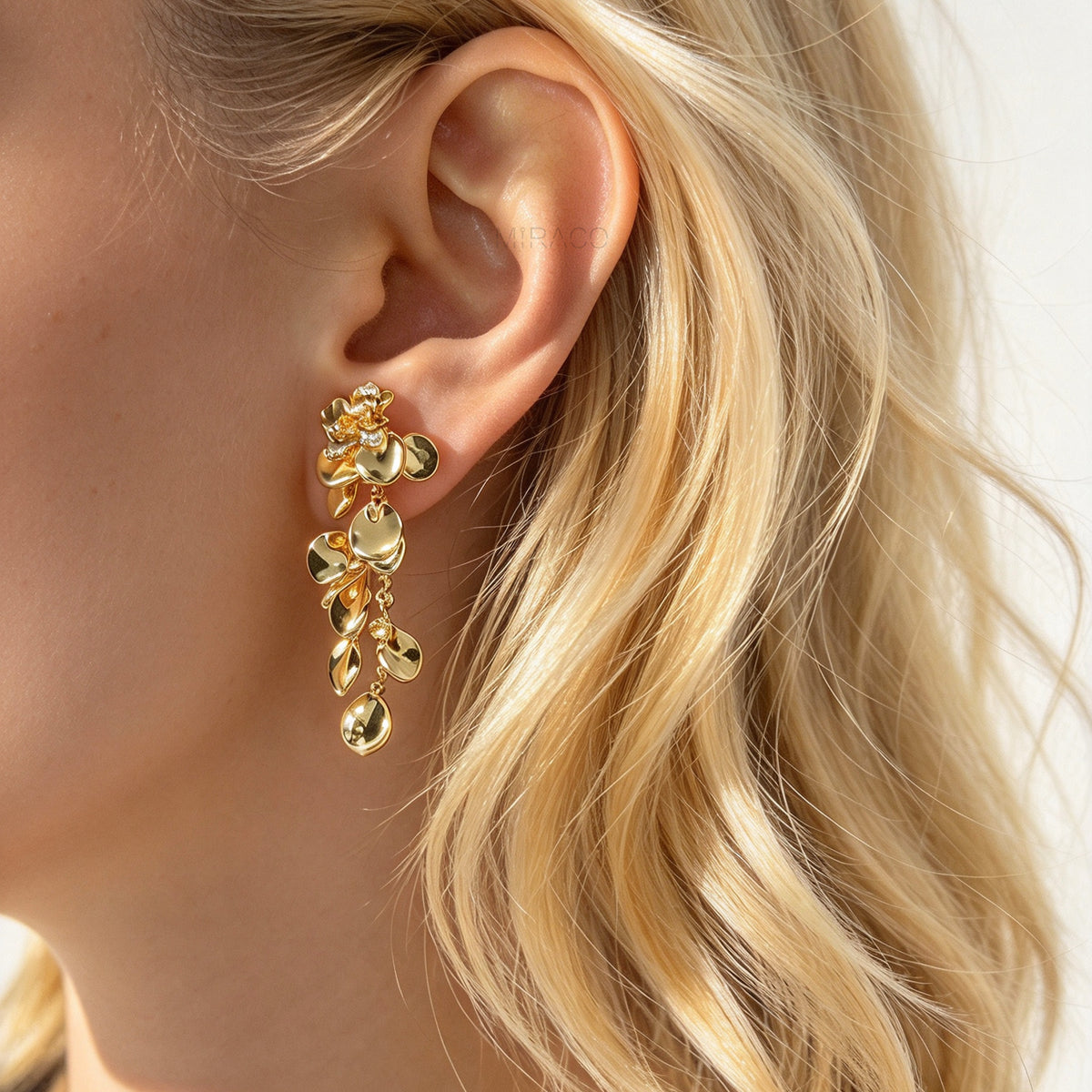 Gold cascading petal drop clip-on earrings with coil-back clips worn on a model's ear.