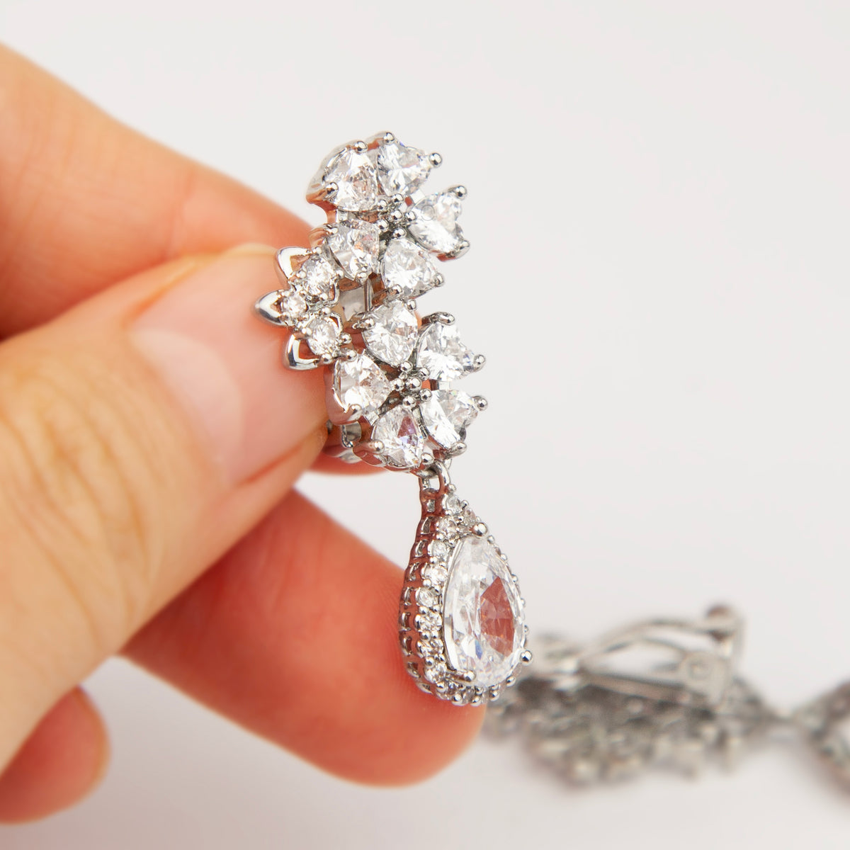 Silver floral cluster clip-on earrings featuring a halo pear-cut cubic zirconia teardrop with paddle backs.