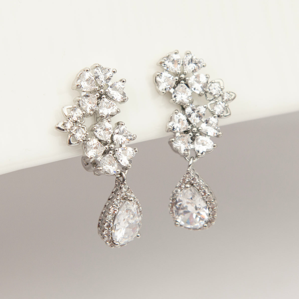 Silver floral cluster clip-on earrings featuring a halo pear-cut cubic zirconia teardrop with paddle backs.