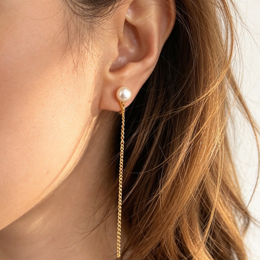 Gold clip-on drop earrings featuring a genuine round freshwater pearl stud with a delicate long chain dangle and invisible coil backs.