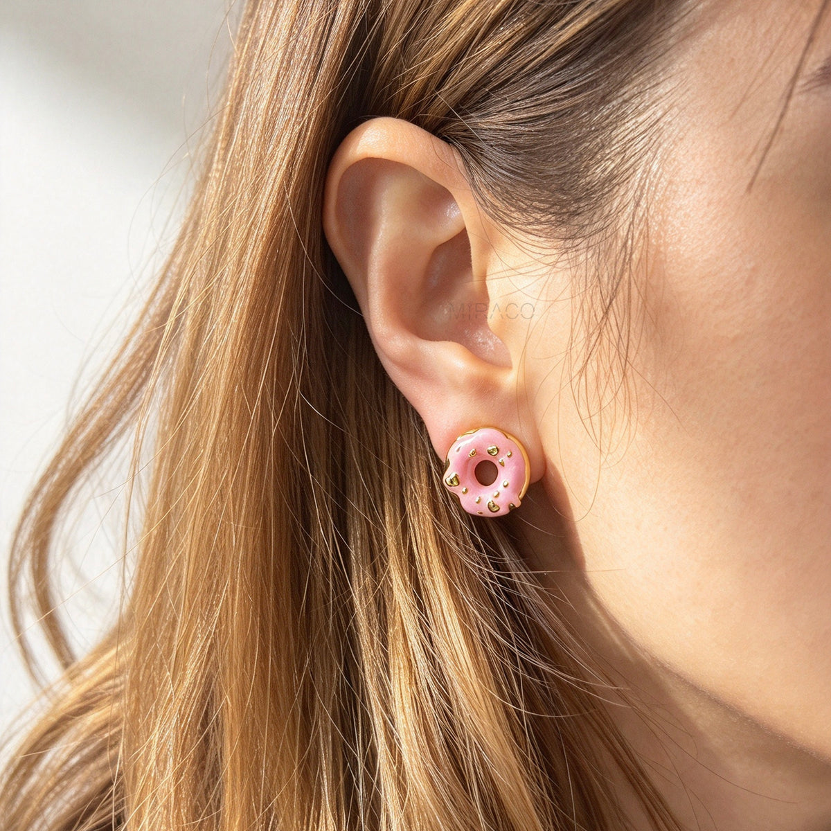 Woman wearing pink enamel donut clip-on earrings with gold sprinkles and coil back non-pierced closure on ear.