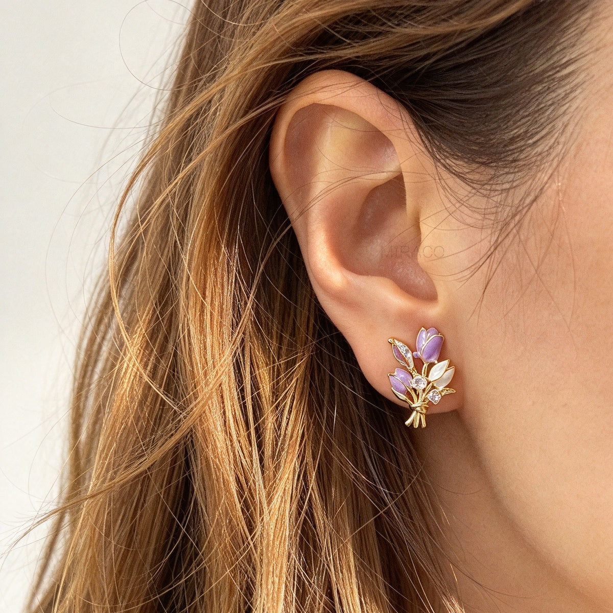 Woman wearing purple and white enamel tulip bouquet clip-on earrings with CZ accents and coil back non-pierced closure in 18K gold plating on ear.