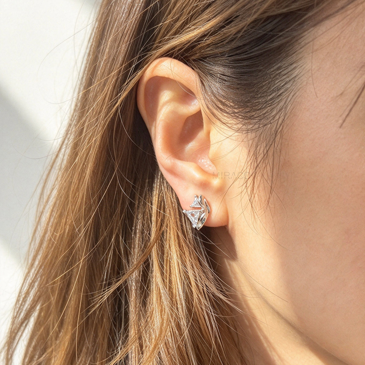Woman wearing silver geometric clip-on earrings set with trillion-cut cubic zirconia and coil back non-pierced closure on ear.