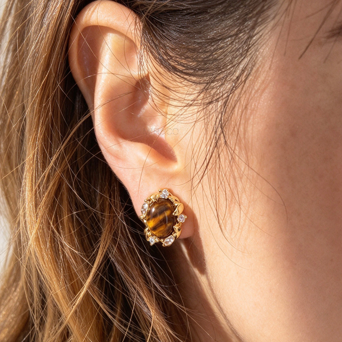 Woman wearing vintage oval tiger's eye cabochon clip-on earrings with cubic zirconia halo accents and coil back non-pierced closure in 18K gold plating on ear.