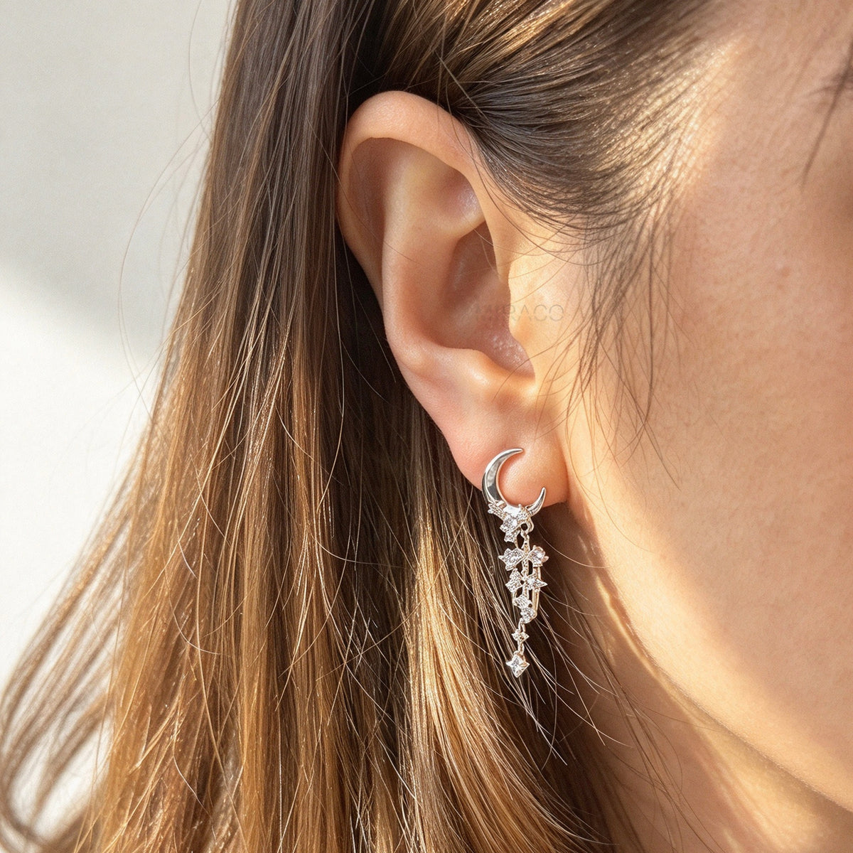 Woman wearing silver celestial crescent moon and starburst dangle clip-on earrings set with cubic zirconia and coil back non-pierced closure on ear.