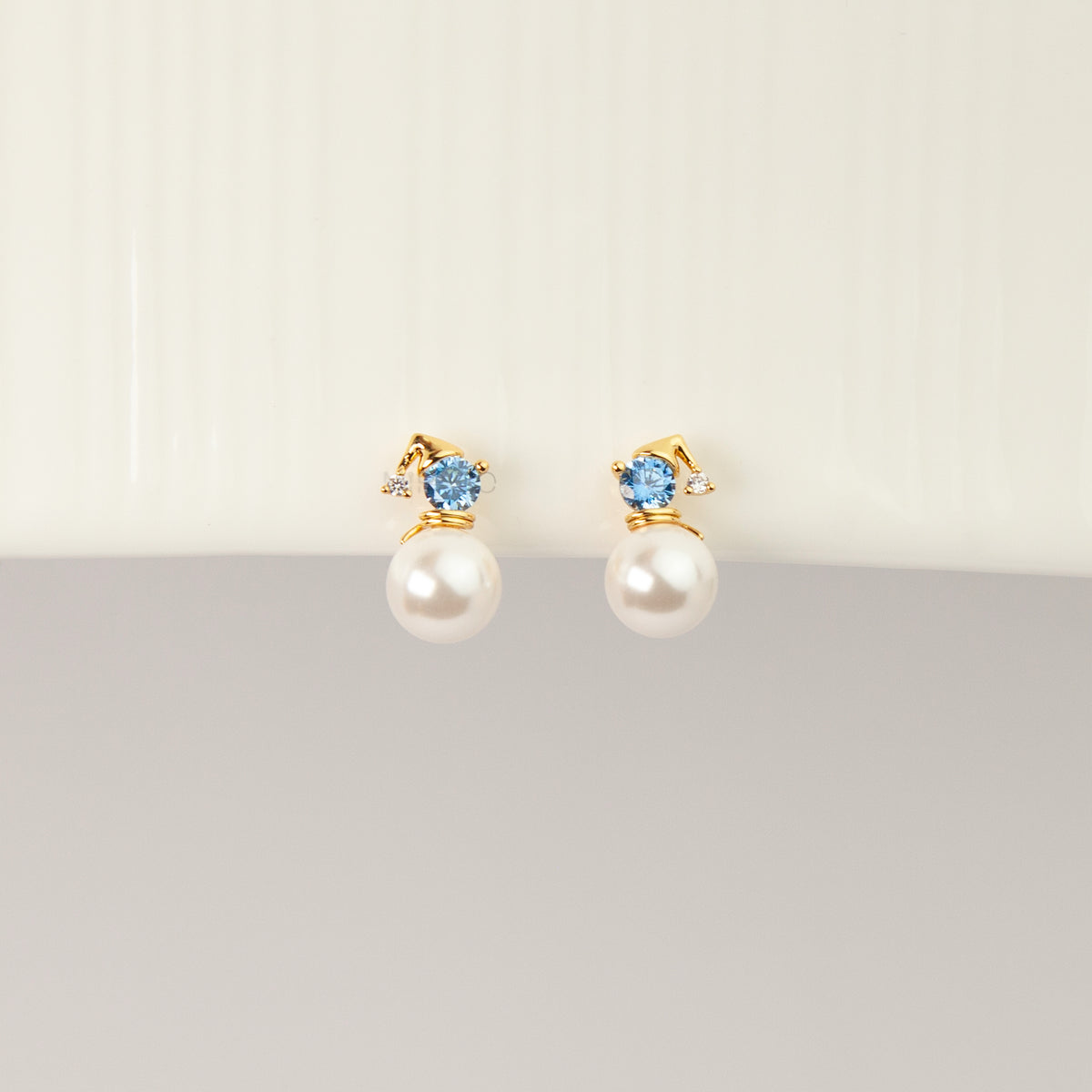 winter snowman pearl drop clip-on earrings featuring a gold hat topper set with a sparkling blue crystal and coil back non-pierced closure