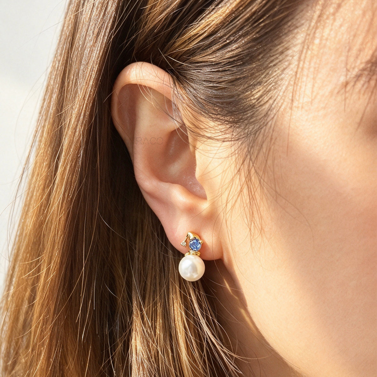 Woman wearing winter snowman pearl drop clip-on earrings featuring a gold hat topper set with a sparkling blue crystal and coil back non-pierced closure on ear.