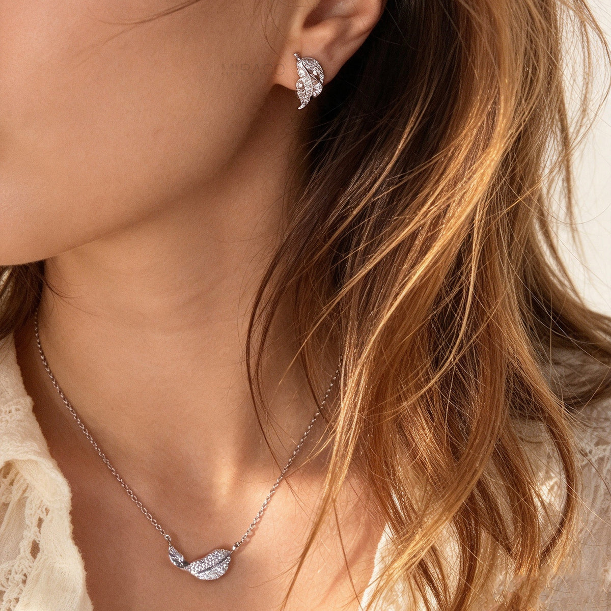 Woman wearing silver pavé crystal feather leaf pendant necklace and matching coil back clip-on earrings for unpierced ears.