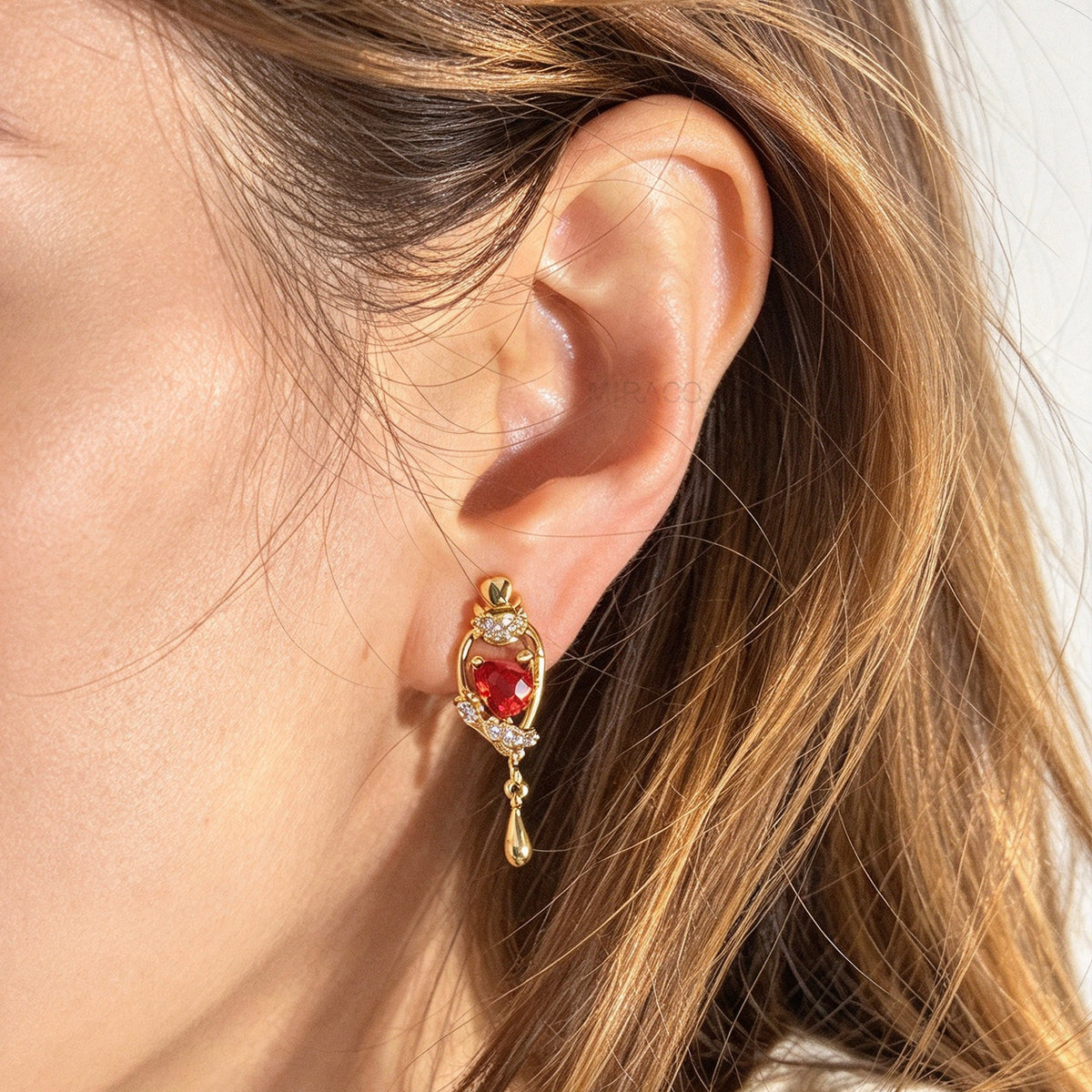 Woman wearing 18K gold-plated royal crimson hat starburst teardrop clip-on earrings with red CZ stone and coil back non-pierced closure on ear.