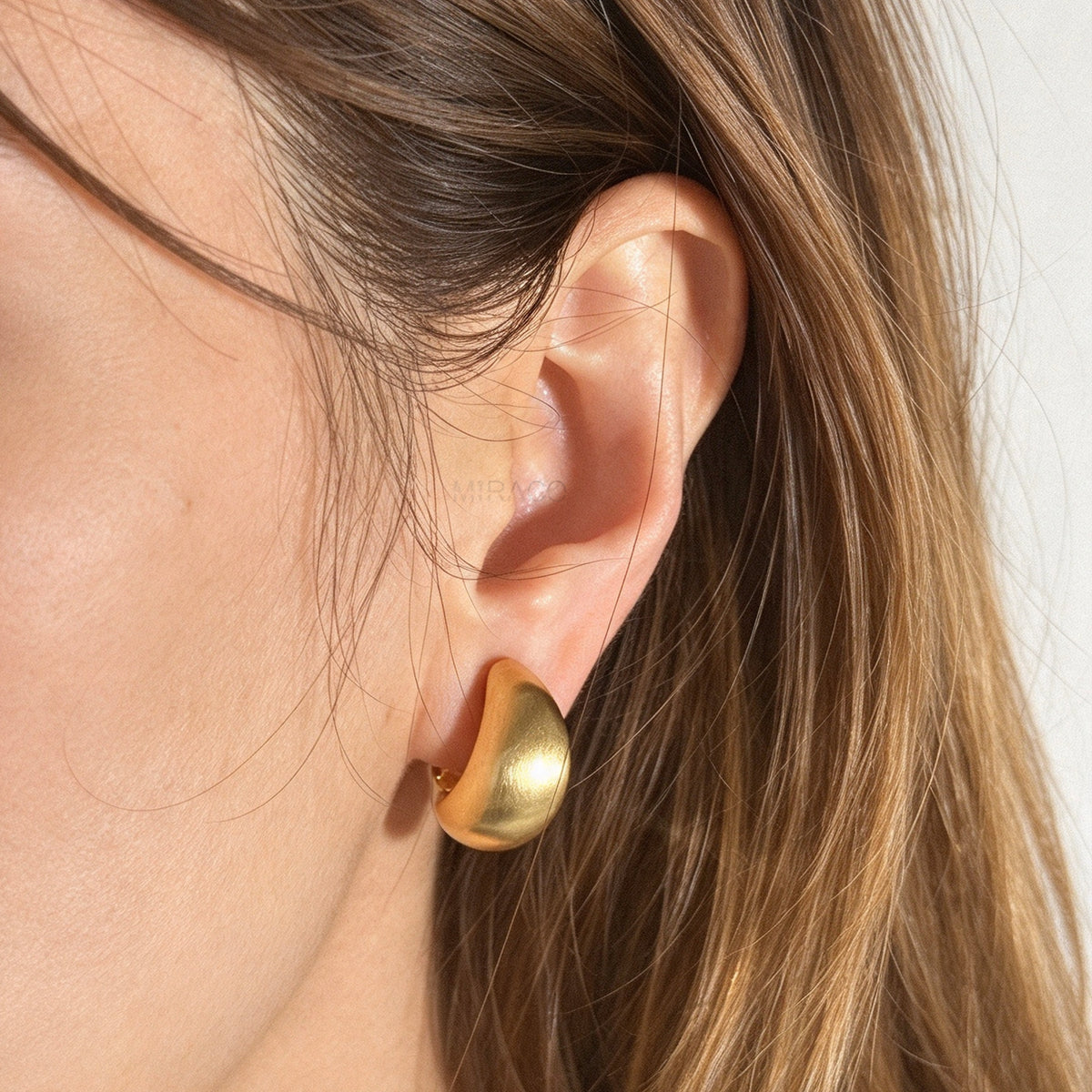 Woman wearing brushed matte gold curved dome huggie clip-on earrings with paddle clip back closure for unpierced ears.