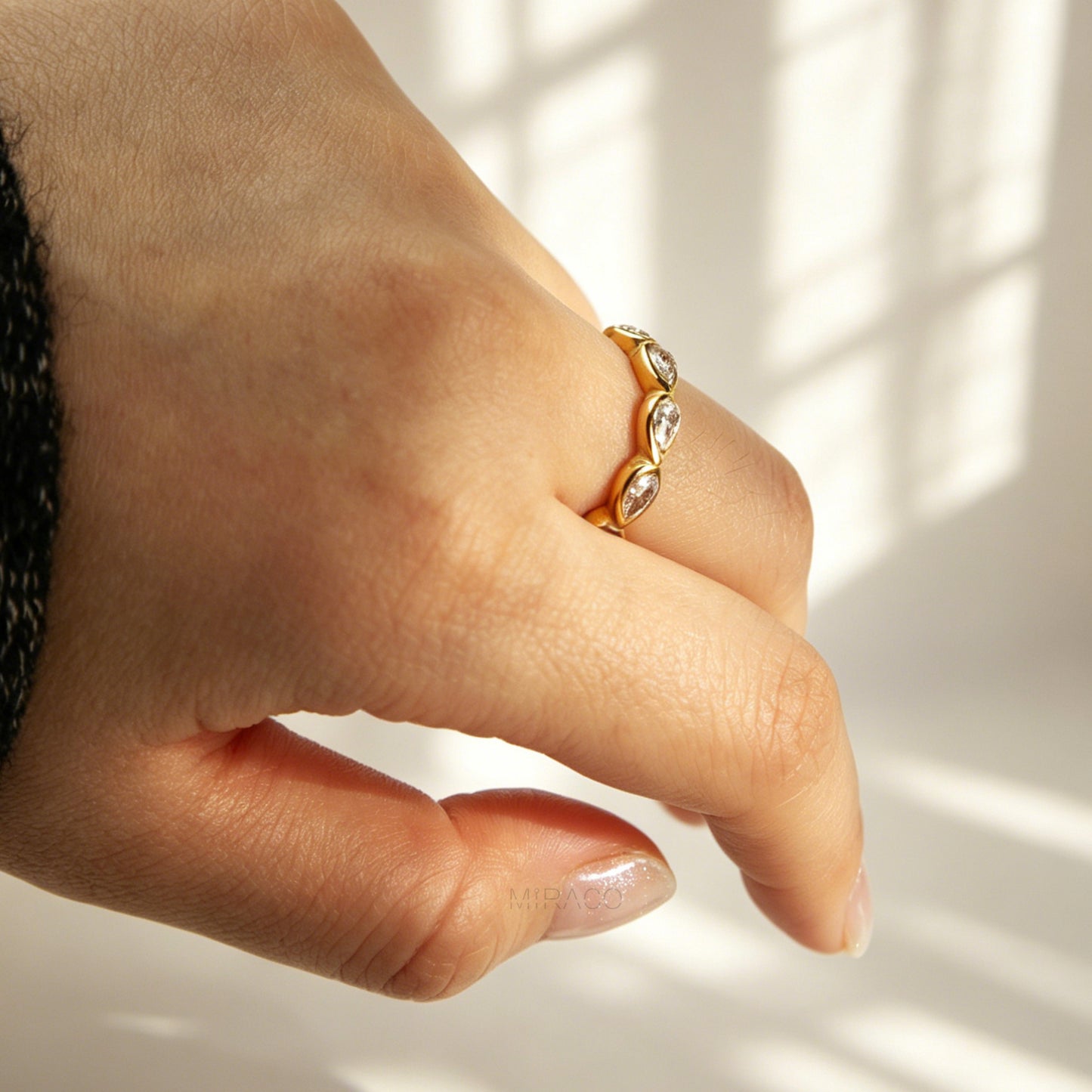 A high-shine gold-toned eternity ring made of stainless steel, featuring a continuous circle of bezel-set pear-cut clear crystals