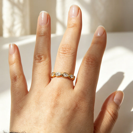 A high-shine gold-toned eternity ring made of stainless steel, featuring a continuous circle of bezel-set pear-cut clear crystals
