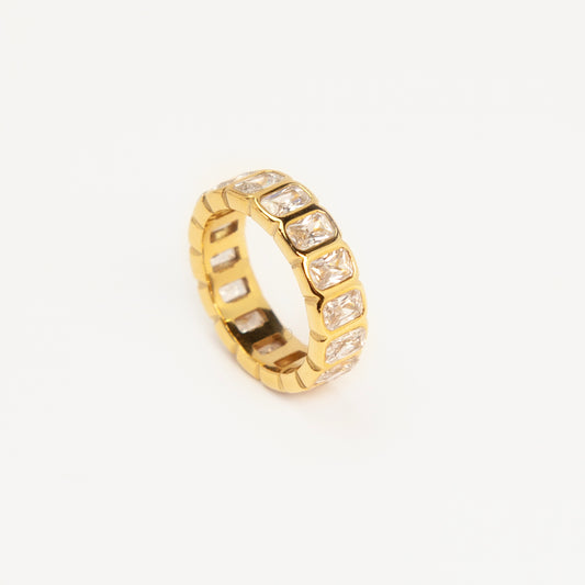 A polished gold-tone stainless steel eternity band ring featuring a continuous row of bezel-set emerald-cut clear crystals