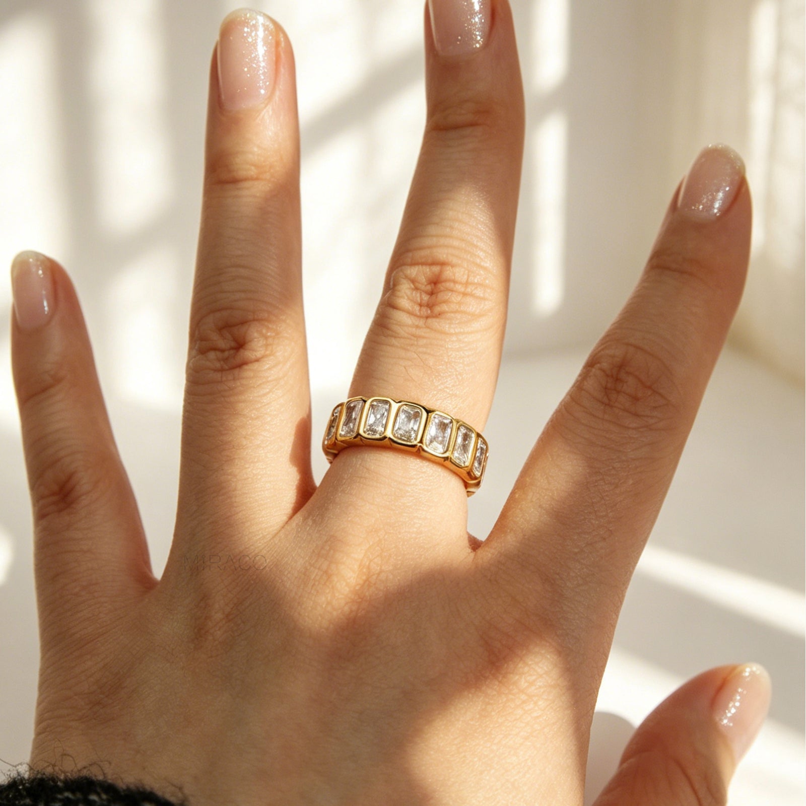 A polished gold-tone stainless steel eternity band ring featuring a continuous row of bezel-set emerald-cut clear crystals